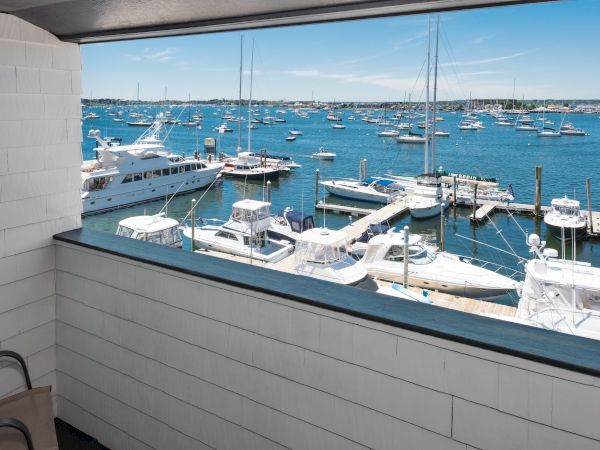 View of a marina with numerous boats docked in the clear blue water, seen from a window or balcony with white paneling.