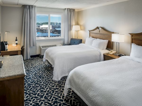 A hotel room with two double beds, a TV, a desk with a lamp, and a window with curtains.