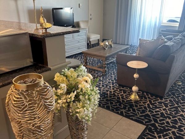 A living room with a sofa, TV, decorative vases with flowers, and a patterned rug. The space has soft lighting and elegant decor.