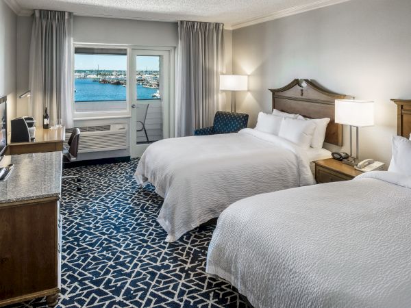 The image shows a hotel room with two beds, a TV, a desk, and a window overlooking a marina with boats and a waterfront view.
