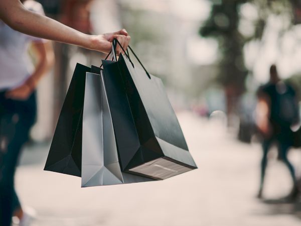 A person is holding three shopping bags on a street with people walking in the background.