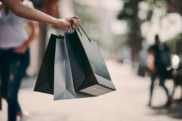 A person is holding three shopping bags on a street with people walking in the background.