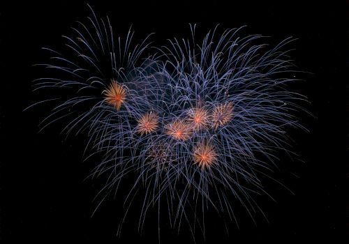 A display of fireworks with vibrant blue and orange bursts against a black sky.