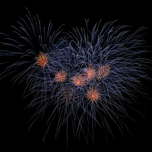 A display of fireworks with vibrant blue and orange bursts against a black sky.