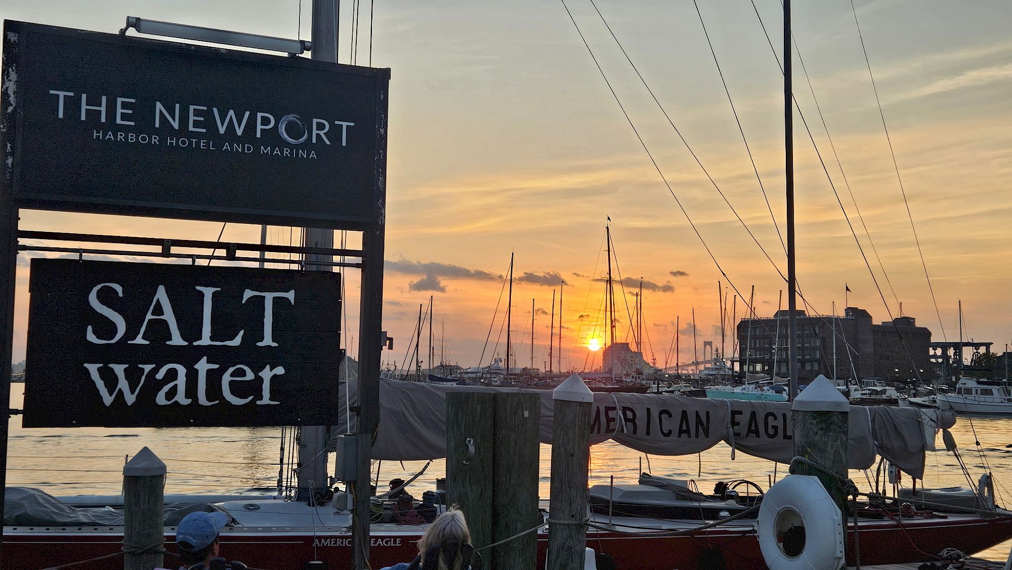A marina scene at sunset with boats, "The Newport Harbor Hotel and Marina," and "Salt Water" signs visible in the foreground.