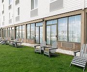 A courtyard outside an apartment building with bright green grass, gravel edging, and rows of gray patio chairs along glass doors.