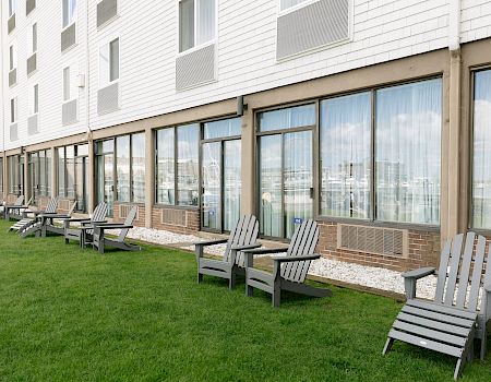 A courtyard outside an apartment building with bright green grass, gravel edging, and rows of gray patio chairs along glass doors.