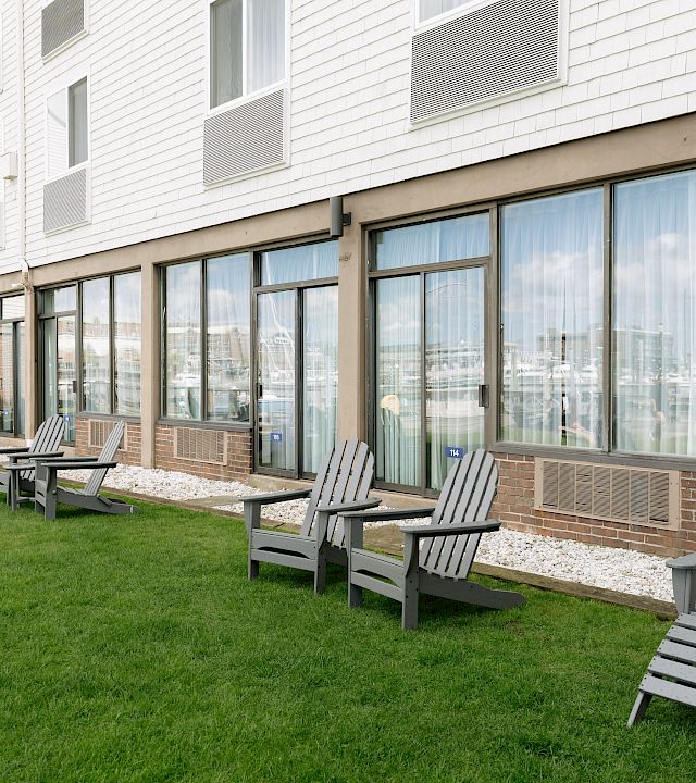 A courtyard outside an apartment building with bright green grass, gravel edging, and rows of gray patio chairs along glass doors.