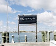 A marina pier sign reads “The Newport Harbor Hotel and Marina,” with blue sky and water in the background.
