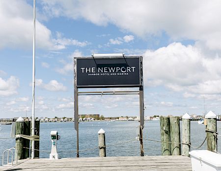 A marina pier sign reads “The Newport Harbor Hotel and Marina,” with blue sky and water in the background.