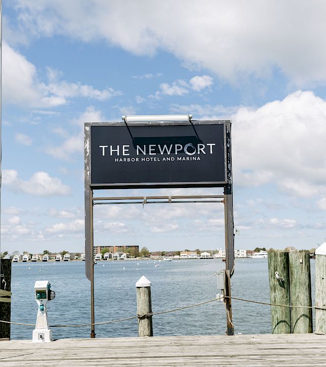 A marina pier sign reads “The Newport Harbor Hotel and Marina,” with blue sky and water in the background.