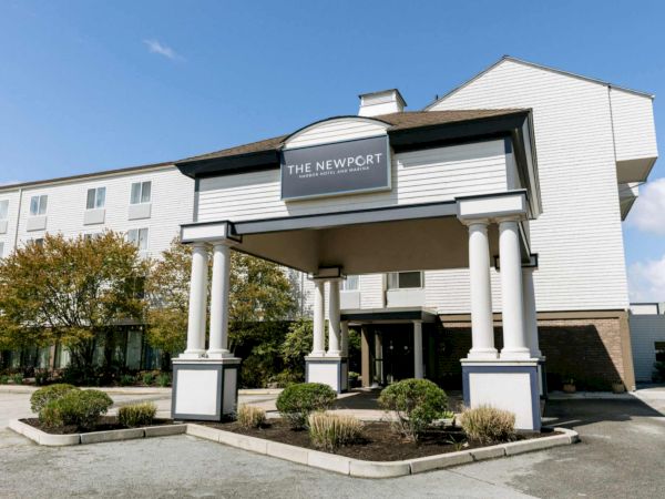 The Newport Harbor Hotel building with a big &ldquo;The Newport&rdquo; sign and white columns under a clear blue sky.