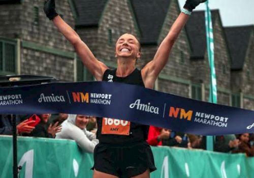 A runner celebrates crossing the finish line with arms raised at the Newport Marathon.