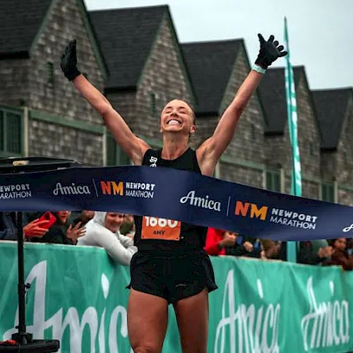 A runner celebrates crossing the finish line with arms raised at the Newport Marathon.