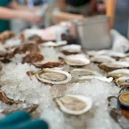 A vendor’s table of oysters on crushed ice with lemon slices and sauce cups in a busy market.